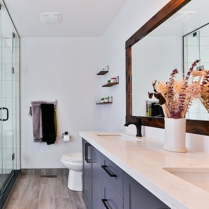 Pristine white bathroom with glass shower and blue cabinet with white countertop and large mirror with wood frame