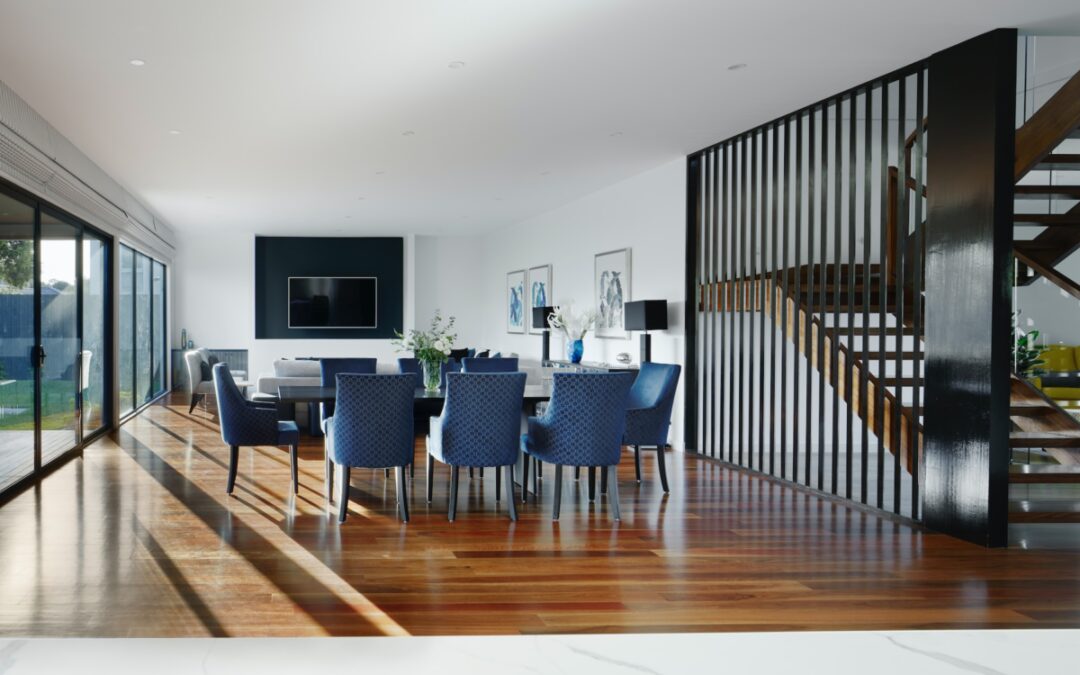 dining table with fashionable blue fabric chairs open to a living room and wood floating stairs to the left.